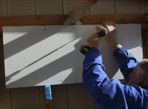 Person drilling drywall onto wooden beams