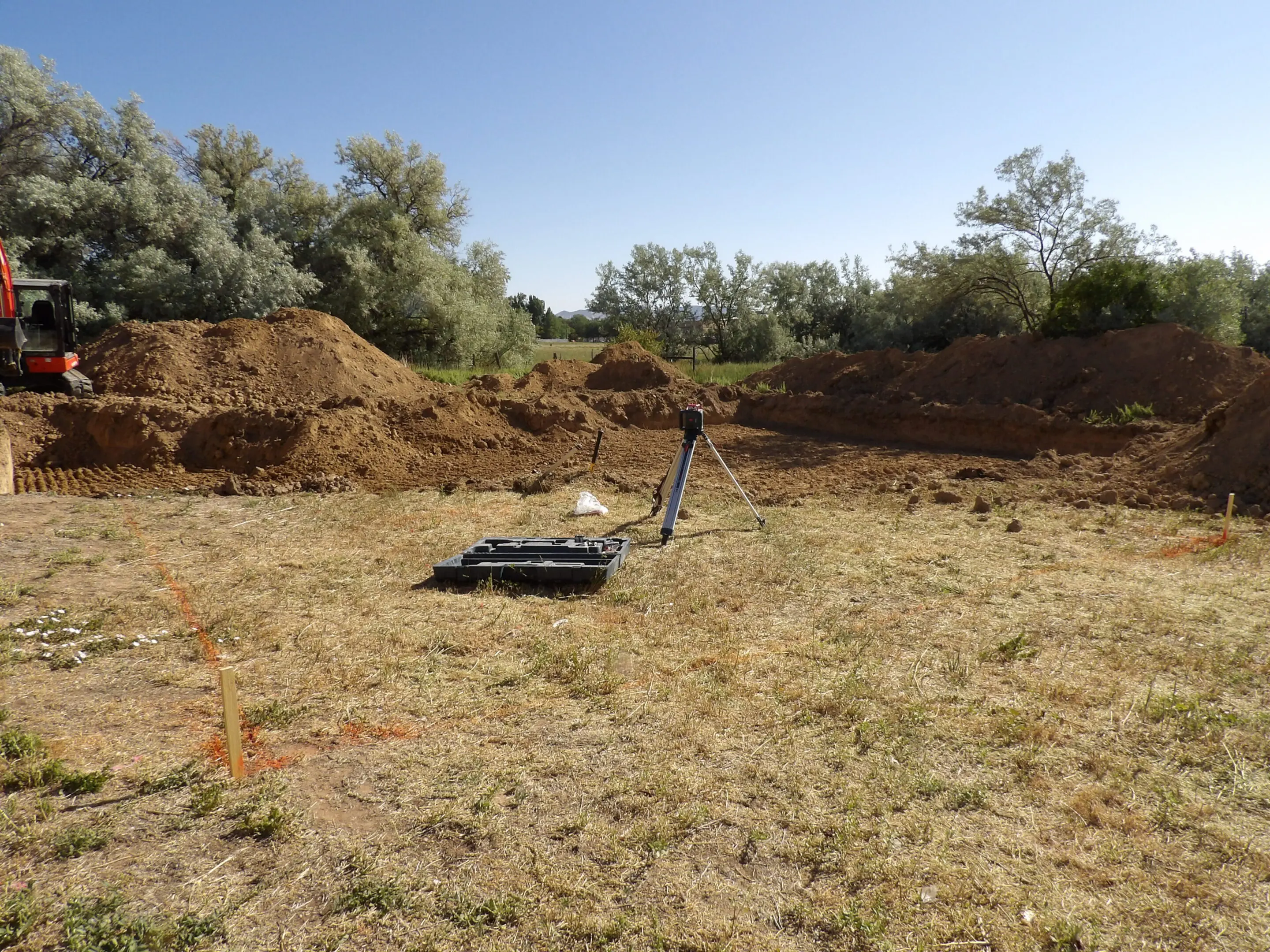 Metal detector placed on dry grassy ground near dirt mounds under clear sky.