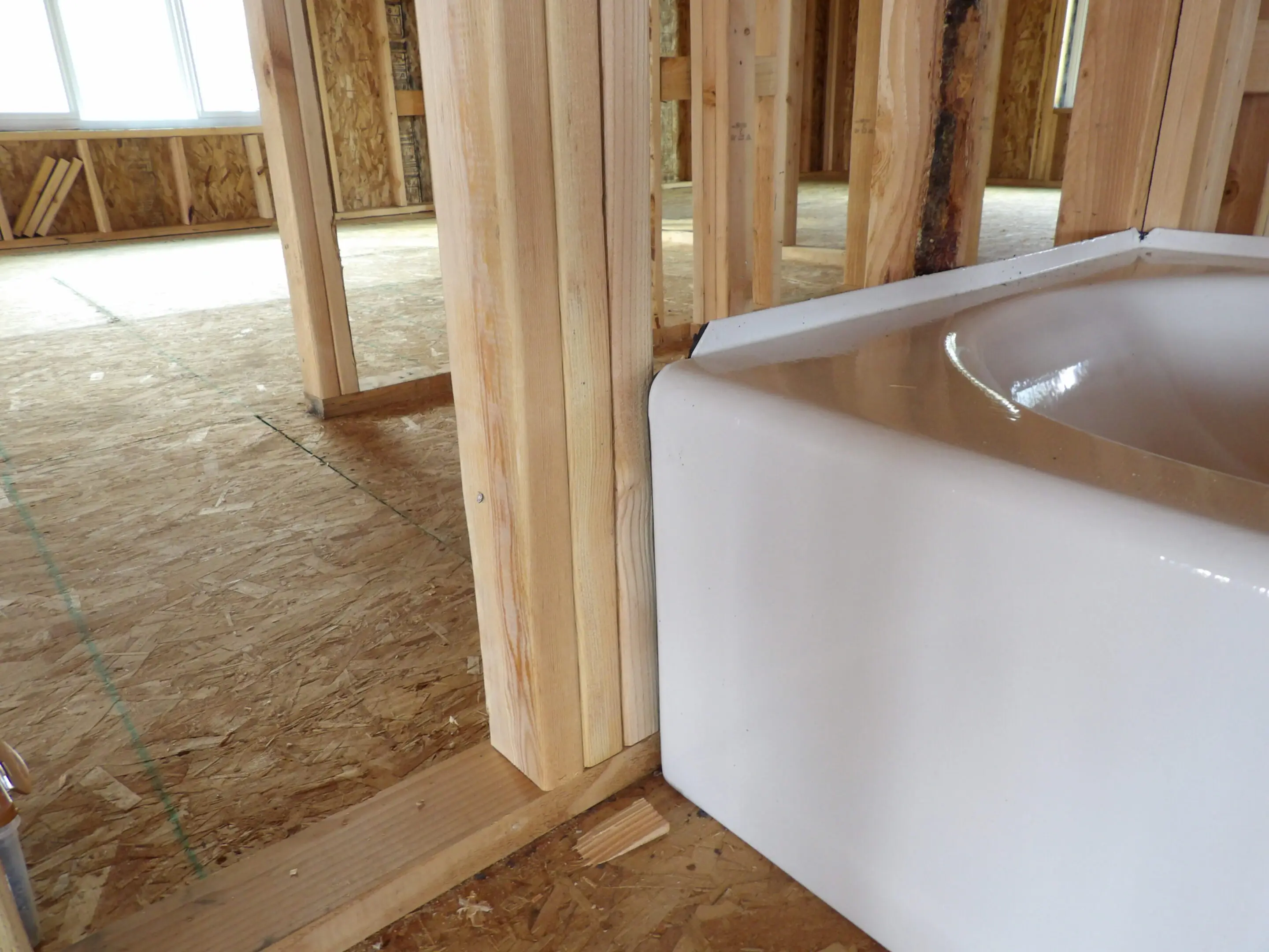 Close-up of a wood-framed wall next to a bathtub in a home under construction.