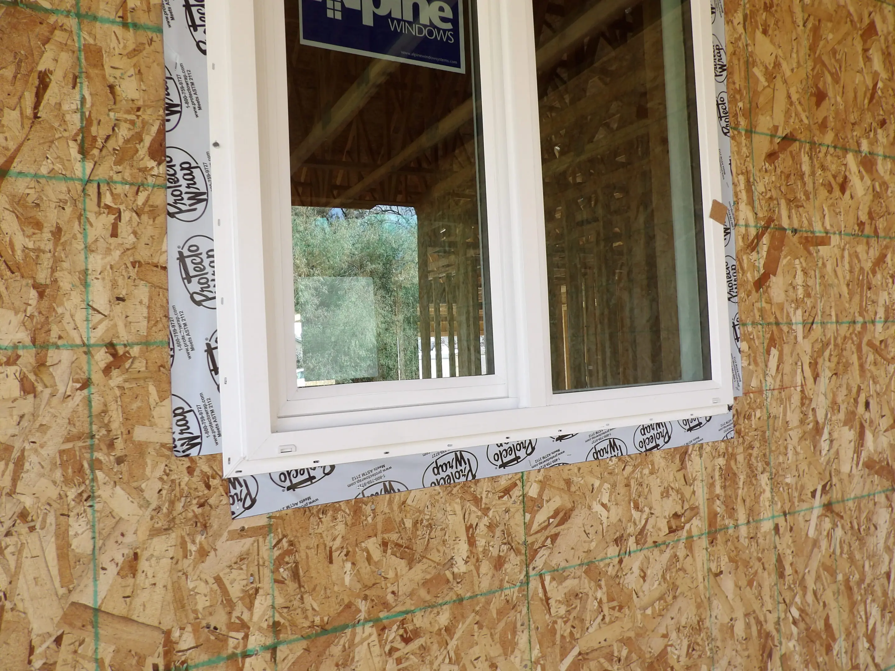 Window installed in an unfinished wooden wall with protective tape around the frame.