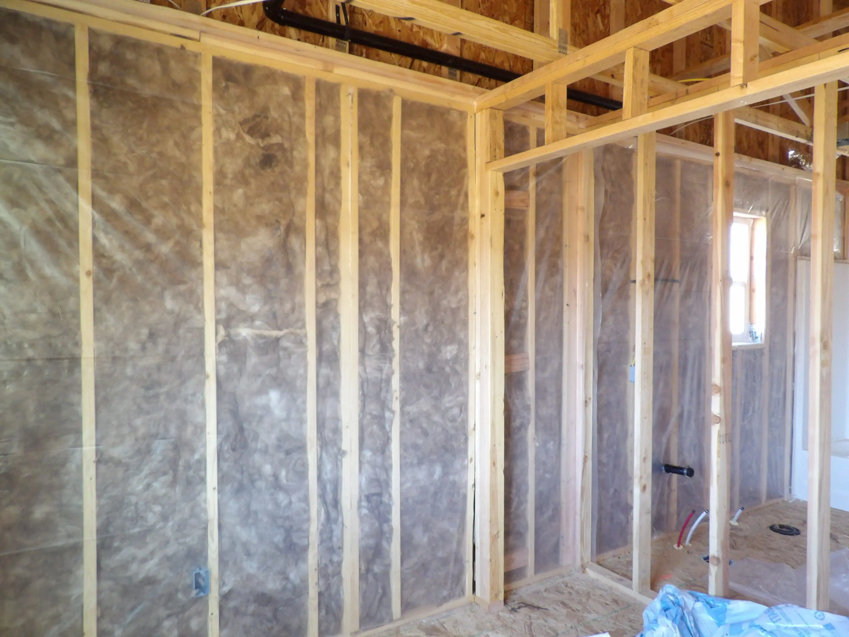 Interior wall insulation installation in progress inside a wooden frame structure.